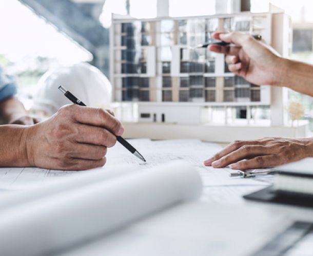 Architekten planen ein Bauprojekt, diskutieren über Pläne und Modelle am Tisch.