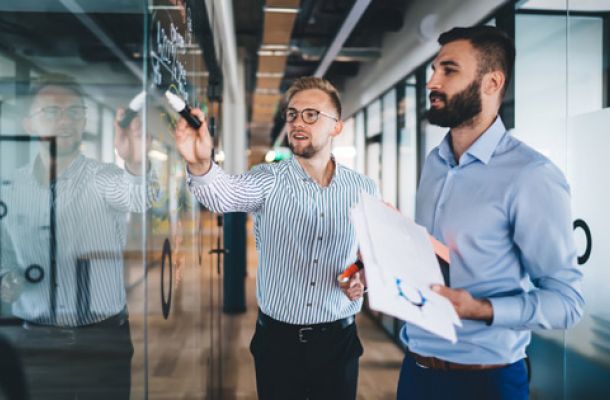 Zwei Geschäftsleute diskutieren und planen Strategien an einer Glaswand im Büro.