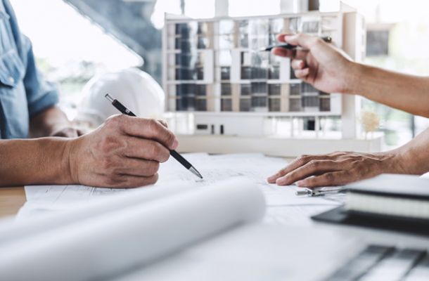 Architekten planen ein Bauprojekt, diskutieren über Pläne und Modelle am Tisch.